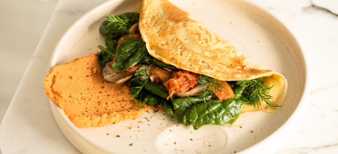 A freshly cooked omelette served on a plate, filled with vegetables and cooked meats.